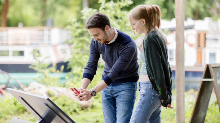 A couple reading an information board using their phone to scan a QR code in order to listen to an audio guide.